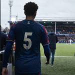 Un jeune joueur de Crystal Palace, vu de dos, entre sur la pelouse d'un stade anglais.