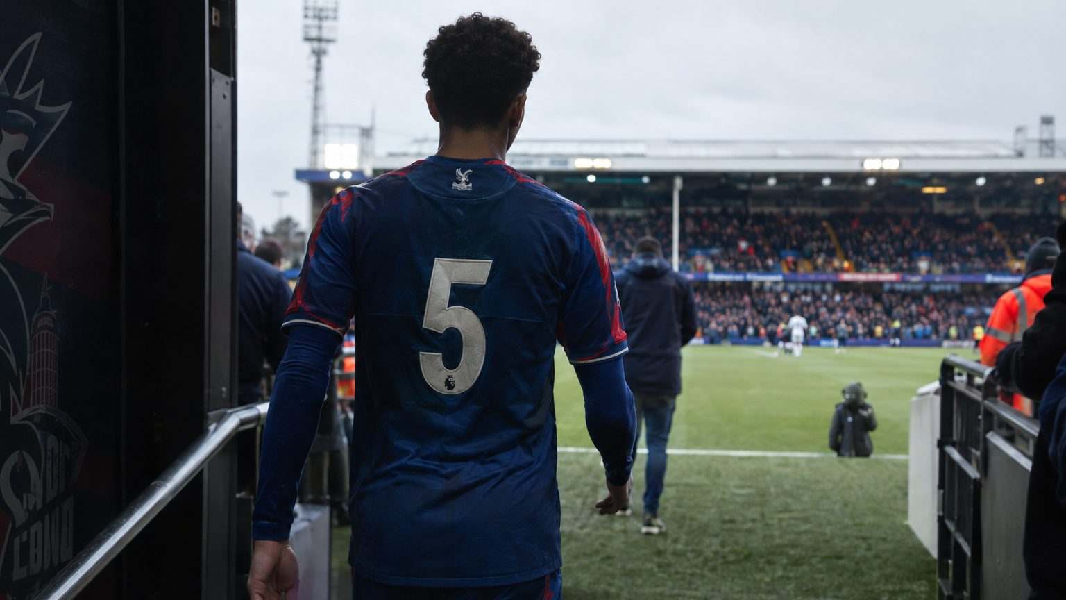 Un jeune joueur de Crystal Palace, vu de dos, entre sur la pelouse d'un stade anglais.
