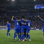 Joueurs de l’équipe de France célébrant une victoire sur la pelouse du Stade de France, public en arrière-plan.